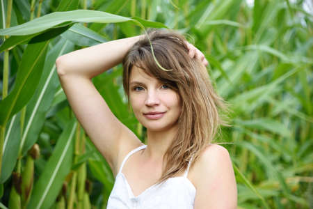 Outdoor photos of young woman in her 30's. Summer season in Poland. Portrait with green corn leafs in the background.の写真素材