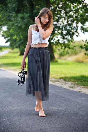 Outdoor photos of young woman in her 30's. Summer season in Poland. Woman walking barefoot on empty road.の写真素材