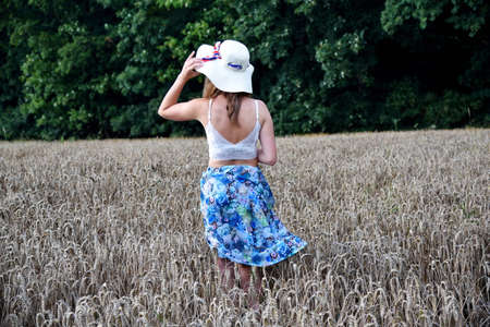 Outdoor photos of young woman in her 30's. Summer season in Poland. Woman with straw hat stands in wheat's field.の写真素材