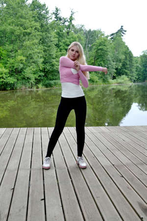 Young and slim woman exercising in park with pond. Polish woman doing some yoga and stretching.の写真素材