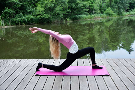 Young and slim woman exercising in park with pond. Polish woman doing some yoga and stretching.の写真素材