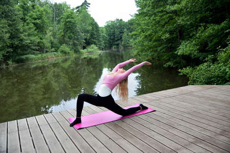 Young and slim woman exercising in park with pond. Polish woman doing some yoga and stretching.の写真素材