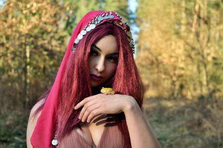 Female model in forest, daytime photo session. Young woman with red hairs, princess with frog.の写真素材