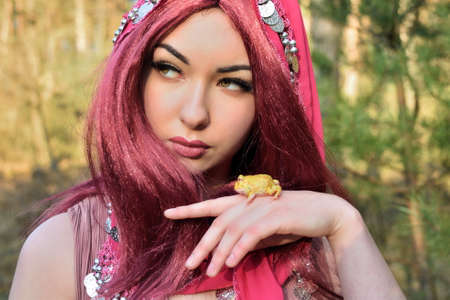 Female model in forest, daytime photo session. Young woman with red hairs, princess with frog.の写真素材