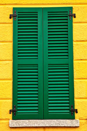 Closed green window shutters on yellow house facade.の写真素材