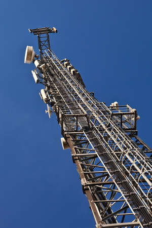 Telecommunication mast with microwave link antennas over a blue sky.