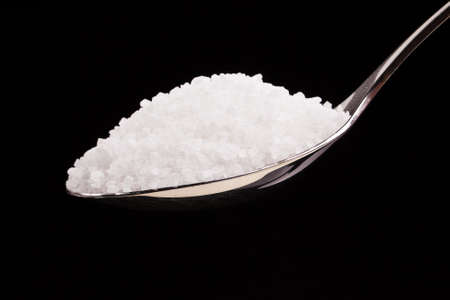 Silver spoon full of white crystal sugar isolated over black background.の写真素材