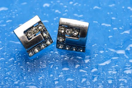 a pair of silver earrings with diamonds on blue background with water dropsの写真素材