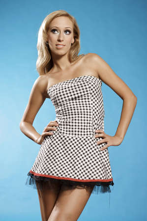 Young blonde woman posing in stylish dress on blue backgroundの写真素材