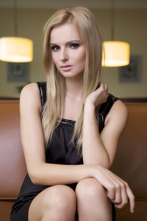 attractive blond woman in black dress sitting on the couchの写真素材