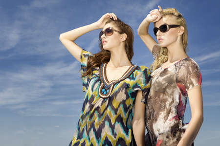 two beautiful brunette and blonde girl in sunglasses on background blue skyの写真素材