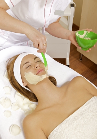 young woman getting beauty skin mask treatment on her face with brushの写真素材