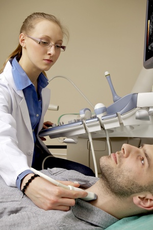 Portrait of young female technician doctor operating ultrasound machine in white dressの写真素材