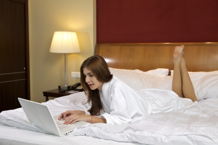 Portrait of beautiful brunette woman with laptop on bed at bedroomの写真素材