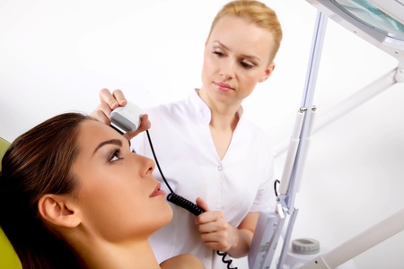 Portrait of attractive beautiful young adult brunette woman having a stimulating facial treatment from a therapist on the table in proffessional clinic spaの写真素材