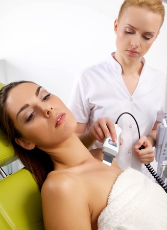 Portrait of attractive beautiful young adult brunette woman having a stimulating facial treatment from a therapist on the table in proffessional clinic spaの写真素材