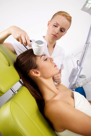 Portrait of attractive beautiful young adult brunette woman having a stimulating facial treatment from a therapist on the table in proffessional clinic spaの写真素材