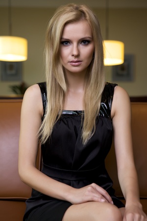 attractive blond woman in black dress sitting on the couchの写真素材