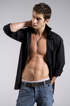 Portrait of muscle man in black shirt and blue jeans posing on a grey backgroundの写真素材