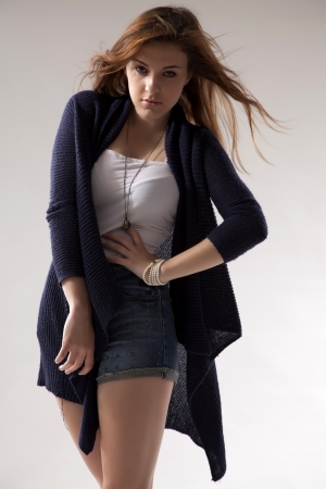 portrait of a beautiful young  brunette woman in blue sweater dress and jeans short on greybackground. Autumn style the fashionの写真素材