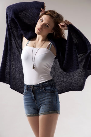 portrait of a beautiful young  brunette woman in blue sweater dress and jeans short on greybackground. Autumn style the fashionの写真素材