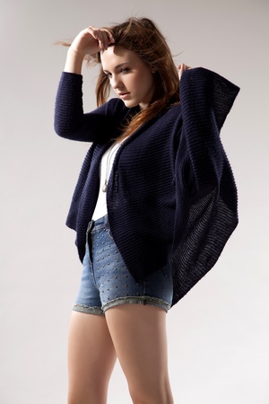 portrait of a beautiful young  brunette woman in blue sweater dress and jeans short on greybackground. Autumn style the fashionの写真素材