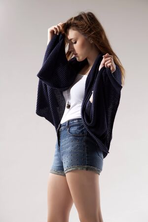 portrait of a beautiful young  brunette woman in blue sweater dress and jeans short on greybackground. Autumn style the fashionの写真素材
