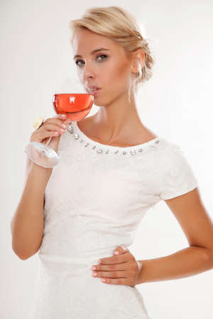 Portrait of happy smiling young attractive blonde woman with glass of red rose wine, in white dress isolated on white backgroundの写真素材