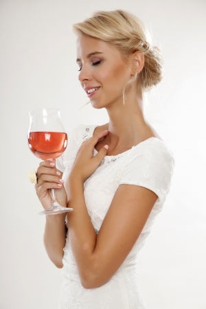 Portrait of happy smiling young attractive blonde woman with glass of red rose wine, in white dress isolated on white backgroundの写真素材