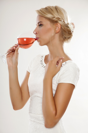 Portrait of happy smiling young attractive blonde woman with glass of red rose wine, in white dress isolated on white backgroundの写真素材