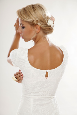 portrait of a beautiful young adult sensuality blonde woman in white elegance dress and flowers in hair isolated on light backgroundの写真素材
