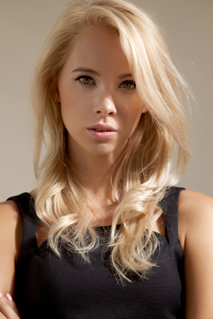 Young pretty woman with beautiful blond hairs in black dress isolated on grey backgroundの写真素材