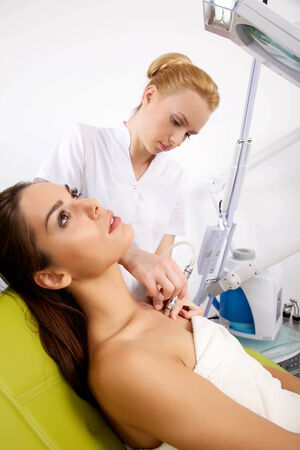 Portrait of attractive beautiful young adult brunette woman having a stimulating facial treatment from a therapist on the table in proffessional clinic spaの写真素材