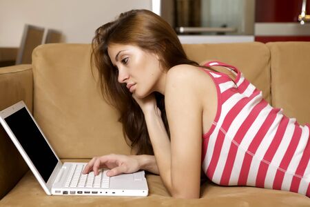 Beautiful young woman lying on a brown sofa with a laptop.の写真素材