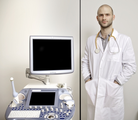 Portrait of young male technician operating ultrasound machine in white dressの写真素材