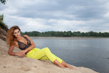 Portrait of attractive sensuality and pretty blonde sexy woman in yellow pants and black bra posing on the beachの写真素材