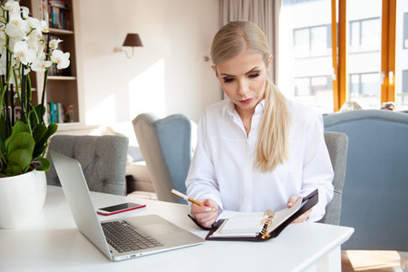 portrait of young adult attractive blonde businesswoman in white shirt working in home officeの写真素材