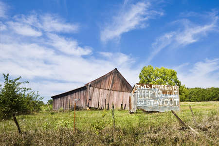 Dilipidated barn sits behind a fence and a warning sign in Kansas の写真素材