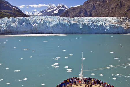 A crowd gathers at the bow of a cruise ship near a glacier の写真素材