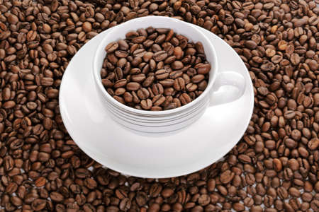 A cup full of coffee beans surrounded by more coffee beansの写真素材