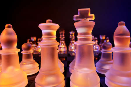 Glass chess on a chessboard lit by a colorful blue and orange light and placed on a glass chessboard
