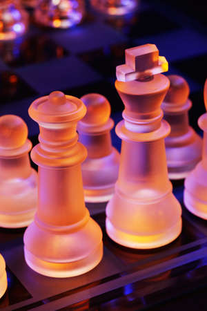 Glass chess on a chessboard lit by a colorful blue and orange light and placed on a glass chessboardの写真素材