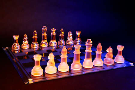 Glass chess on a chessboard lit by a colorful blue and orange light and placed on a glass chessboardの写真素材