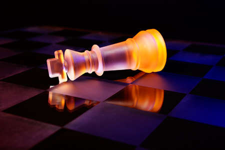 Glass chess on a chessboard lit by a colorful blue and orange light and placed on a glass chessboardの写真素材