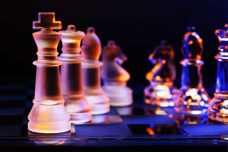 Glass chess on a chessboard lit by a colorful blue and orange light and placed on a glass chessboardの写真素材
