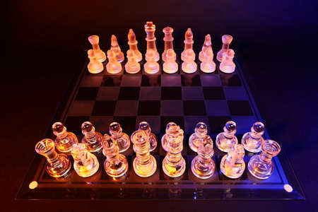 Glass chess on a chessboard lit by a colorful blue and orange light and placed on a glass chessboardの写真素材