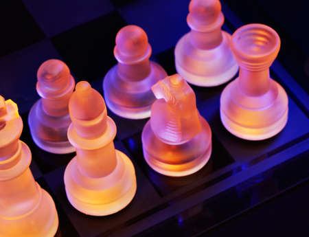 Glass chess on a chessboard lit by a colorful blue and orange light and placed on a glass chessboardの写真素材