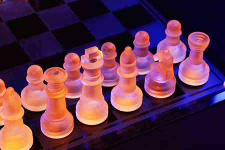 Glass chess on a chessboard lit by a colorful blue and orange light and placed on a glass chessboardの写真素材