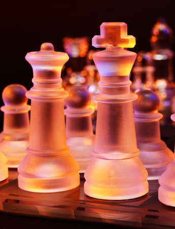 Glass chess on a chessboard lit by a colorful blue and orange light and placed on a glass chessboardの写真素材
