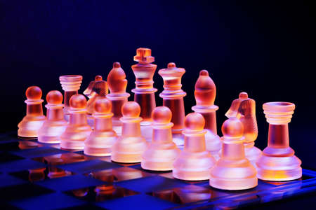 Glass chess on a chessboard lit by a colorful blue and orange light and placed on a glass chessboardの写真素材